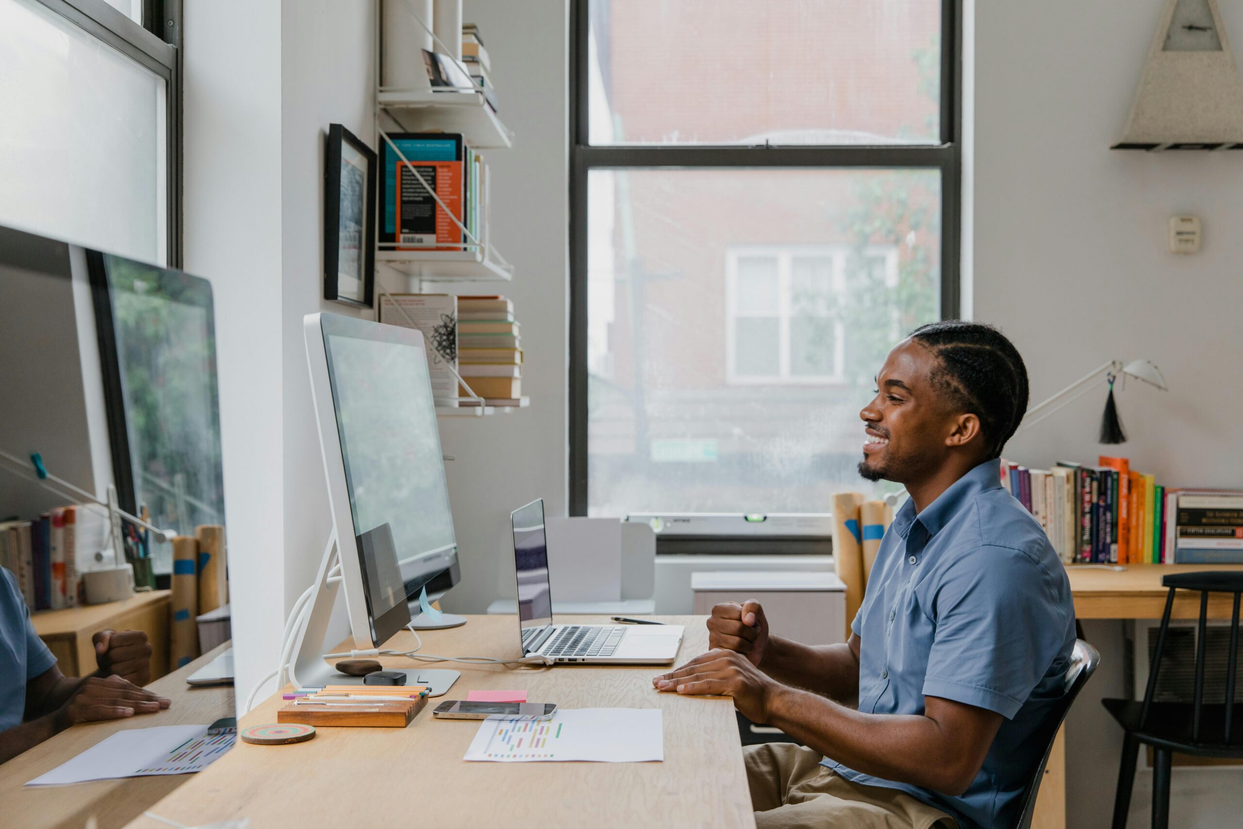 A man with braided hair works on a laptop in a modern home office setting.